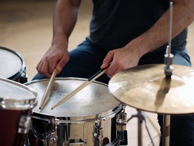 Close-up of man sitting behind drum kit and playing drums during rehearsal